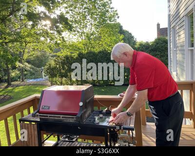 L'homme senior prépare de la viande à placer sur son barbecue Weber classique situé sur notre terrasse en bois d'arrière-cour, USA Banque D'Images