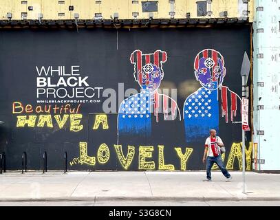 Un homme noir portant un t-shirt drapeau norvégien marchant par l'art de rue annonçant le projet de noir de while.Homme afro-américain regardant par-dessus son épaule comme s'il était suivi. Banque D'Images