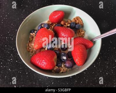 Le petit-déjeuner est composé de muesli avec des noix mélangées, des bleuets et des fraises entières, présentés sur un comptoir de cuisine tacheté de noir Banque D'Images