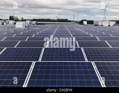 Toit avec rangées de panneaux solaires et éoliennes en arrière-plan Banque D'Images