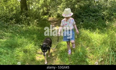 Les jours d'été - petite fille dans chapeau de paille marchant son chien Banque D'Images