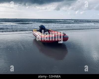 un bateau gonflable motorisé se trouve dans l'eau peu profonde de la plage et des nuages sombres peuvent être vus dans le ciel Banque D'Images