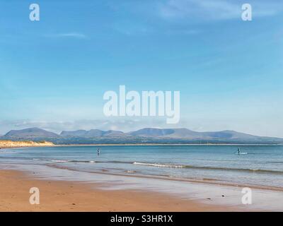 Baignade et paddle-board au large de la côte d'Anglesey sur la plage de Newborough avec la chaîne de montagnes de Snowdonia en arrière-plan, royaume-uni, fin été, 2021 Banque D'Images