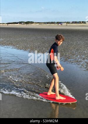 Garçon de douze ans sur un skimboard West Wittering Beach, Angleterre. Banque D'Images