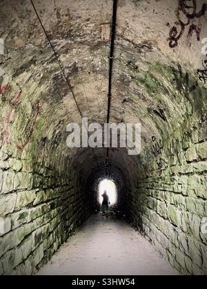 Silhouette anonyme traversant un sous-passage sombre qui simbolise la lumière à l'extrémité du tunnel Banque D'Images