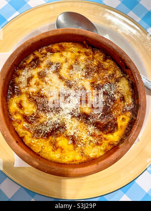 Moussaka (plat grec traditionnel) dans un bol en terre cuite sur une assiette jaune avec cuillère et nappe à carreaux. Banque D'Images