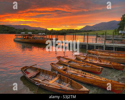Bateaux à rames amarrés et ferry à Keswick, dans le district du lac, contre le soleil couchant Banque D'Images