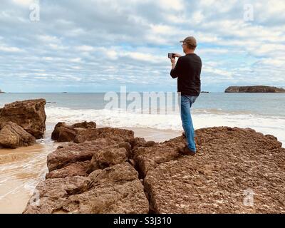 Homme prenant une photo de la côte sur son téléphone Banque D'Images