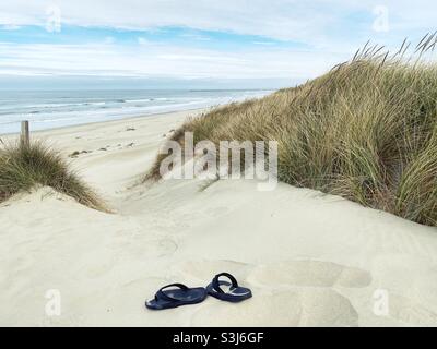 Une paire de tongs noires dans le sable des dunes de l'Oregon à Florence, Oregon. Banque D'Images