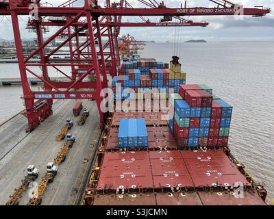 Couvercles de trappe du récipient partiellement chargé avec des conteneurs. Le navire est amarré le long du terminal portuaire de Ningbo, en Chine, équipé d'une grue et de camions. Banque D'Images