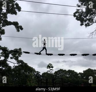 Fille marchant à travers le pont de corde supérieur d'arbre en haut dans le ciel à Go APE Banque D'Images