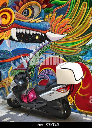 Un scooter de livraison de nourriture garée devant une fresque d'un dragon stylisé, WAN Chai, île de Hong Kong Banque D'Images