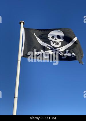 Le crâne de pirate et les crossones crosseds crossaient le drapeau des épées qui flopping dans le vent Banque D'Images