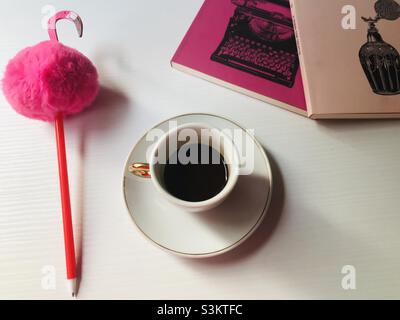 Une tasse de café expresso, quelques livres roses et un stylo rose flamant sur une table blanche. Banque D'Images