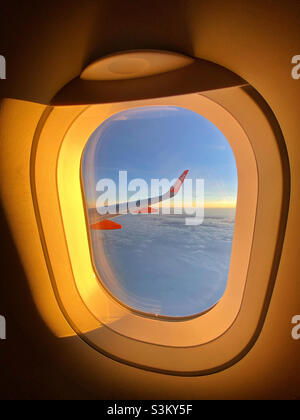 Une vue au-dessus des nuages - des milliers de pieds au-dessus du sol.Vue au lever/coucher du soleil d'une fenêtre EasyJet et d'une aile d'avion.Vous partez en vacances ou vous y retournerez ?Photo ©️ COLIN HOSKINS. Banque D'Images