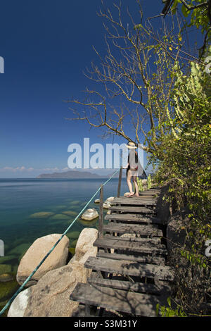 Une jeune femme se dresse sur un escalier en bois donnant sur les eaux tranquilles du lac Malawi. Banque D'Images