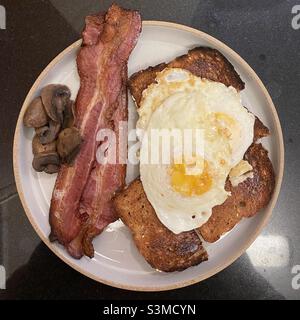 Assiette de petit déjeuner avec bacon frit, œufs sur Easy, toasts et champignons Banque D'Images