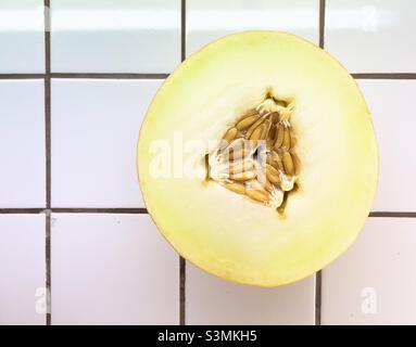 Un demi-melon canari montrant les pépins au centre, reposant sur un plan de travail en carrelage blanc. Banque D'Images