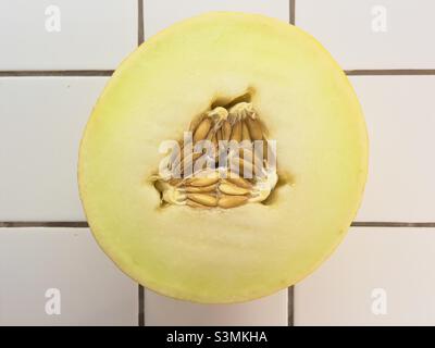 Un demi-melon canari montrant une coupe transversale avec les pépins ou les graines dans l'arrangement triangulaire caractéristique, reposant sur un plan de travail blanc carrelé Banque D'Images