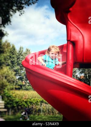 Petite fille portant des lunettes de prescription rose descendant une diapositive Banque D'Images