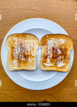 Deux tranches de pain grillé avec beurre sur une assiette blanche Banque D'Images