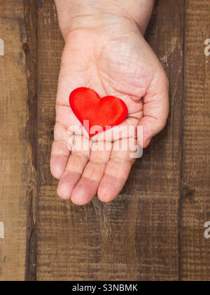 Paume de main bosse d'une femme âgée se trouve sur un fond de table en bois et tient une figure en forme de coeur en couleur rouge, espace de copie. Banque D'Images