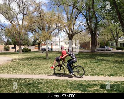 Deux garçons d'âge scolaire moyen font du vélo aux États-Unis, dans le parc public de Springtime. Banque D'Images