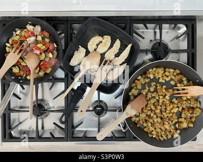 Regarder vers le bas sur les poêles à frire avec les légumes et la cuisson du poulet sur une cuisinière à gaz Banque D'Images