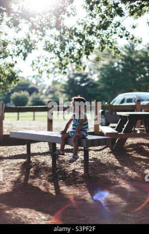 Jeune fille assise sur un banc de parc lors d'une chaude journée d'été baignée de soleil Banque D'Images