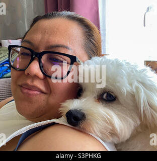 Dame avec un chien cavapoo qui se coud assis sur un canapé. Banque D'Images