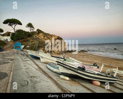 Vue sur le coucher du soleil avec des bateaux garés sur une plage à Olhos de Agua, Algarve, Portugal. Banque D'Images