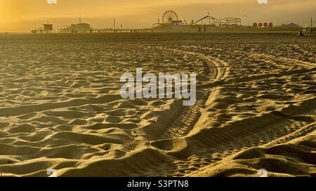 Vue sur le sable en fin d'après-midi, lumière dorée, sur la plage de Santa Monica avec l'accent sur la jetée silhouetée au loin Banque D'Images