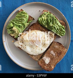 Petit-déjeuner avec pain grillé à l'avocat au grain entier et un œuf frit sur une assiette en céramique grise Banque D'Images