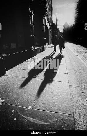Couple marchant le long de Royal Mile à Édimbourg, rétroéclairé par le soleil de la fin de l'après-midi et jetant de longues ombres Banque D'Images
