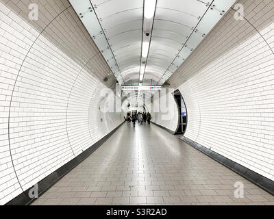 Vue sur un long tunnel blanc à la station de métro Tottenham court Road London en direction des trains Central Line. Banque D'Images