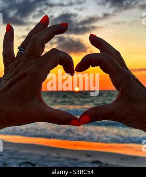 Coucher de soleil à travers les mains en forme de coeur à la plage de Bean point sur l'île Anna Maria, en Floride États-Unis Banque D'Images