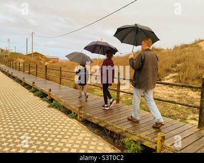 Famille marchant le long d'une promenade sous la pluie avec des parasols Banque D'Images