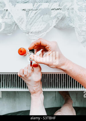 Femme peignant ses orteils rouges reposant sur le seuil de la fenêtre Banque D'Images