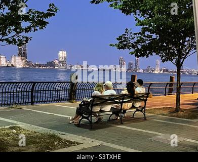 Personnes assises sur un banc au crépuscule surplombant l'East River à Manhattan New York, Etats-Unis Banque D'Images