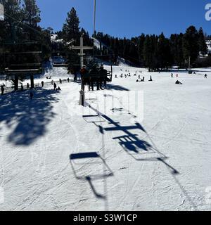 Des cavaliers anonymes sont en ascension au Snow Summit en Californie, qui projette de grandes ombres sur les pistes couvertes de neige en contrebas, avec d'autres skieurs et snowboarders sur la montagne Banque D'Images