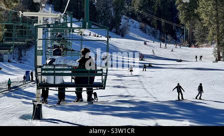 Des passagers anonymes sont en télésiège au Snow Summit en Californie, avec d'autres skieurs et snowboardeurs sur des pistes enneigées Banque D'Images