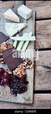 Planche en bois de fromage et de craquelins avec raisins, noix, céleri et chutney. Banque D'Images