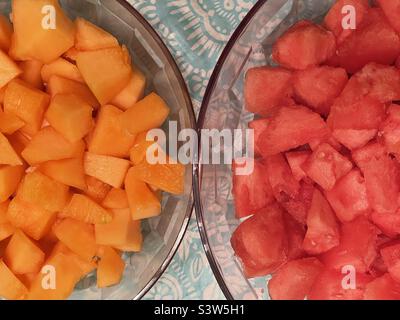 Deux grands bols, côte à côte, s'assoient sur un plan d'examen rempli de fruits frais coupés. Un bol contient une délicieuse cantaloup et l'autre pastèque juteuse. Couleurs naturelles organiques de l'orange et du rouge. Banque D'Images