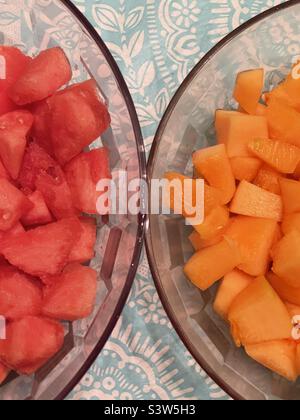 Deux grands bols, côte à côte, s'assoient sur un plan d'examen rempli de fruits frais coupés. Un bol contient une délicieuse cantaloup et l'autre pastèque juteuse. Couleurs naturelles organiques de l'orange et du rouge. Banque D'Images