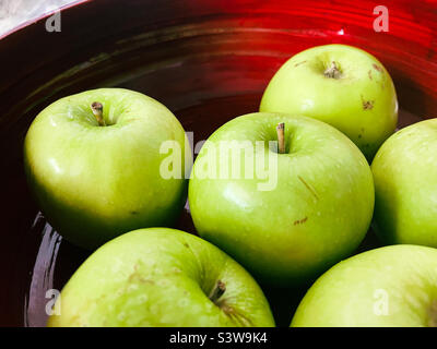 Une collection de pommes vertes Granny Smith reposant dans un bol rouge vif Banque D'Images