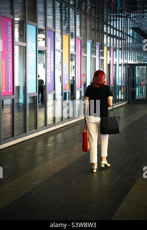 Vue arrière de la dame aux cheveux rouges marchant dans un environnement coloré de la ville de Birmingham pendant les Jeux du Commonwealth 2022 Banque D'Images