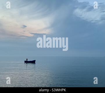 Bateau et pêcheur sur mer brumeux calme Banque D'Images