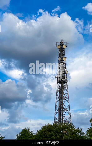 Un mât de télécommunication, la télévision antennes la technologie sans fil contre ciel nuageux sur les haies vertes Banque D'Images