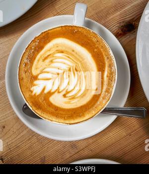 « Latte Lunch » Latte avec un motif complexe au milieu d'une table, entouré d'autres assiettes Banque D'Images