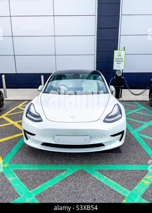 Tesla blanc modèle 3 branché à une station de charge électrique Banque D'Images